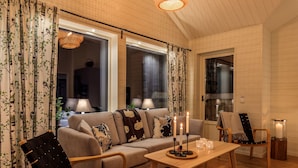 A cozy living room with a sofa, armchair, and coffee table, featuring a hanging light fixture and candles. - Fjällstugan (Bruksvallarna)