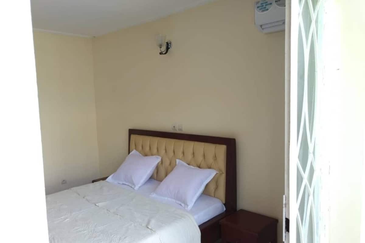A bedroom with a bed, two pillows, a nightstand, and a wall-mounted air conditioner.