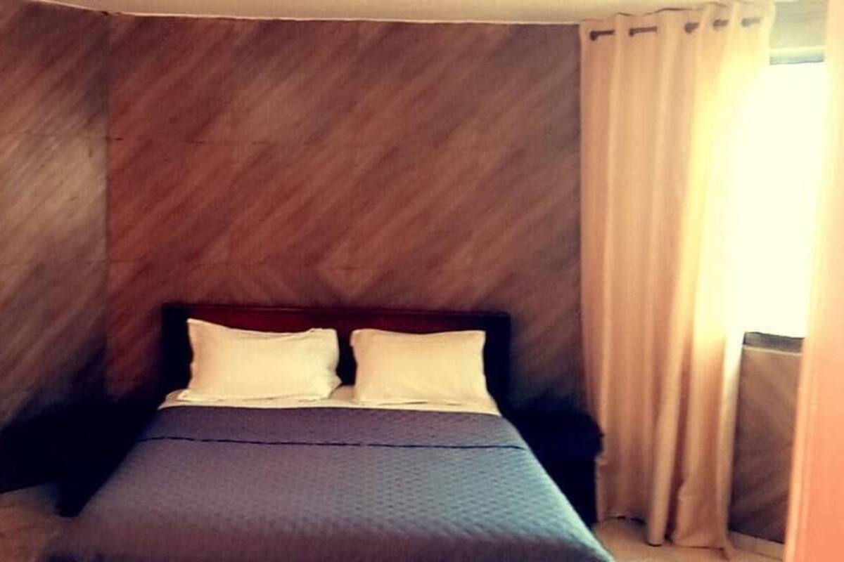 A room with a bed, wooden walls, and a window with curtains.