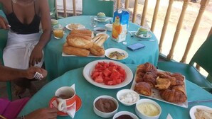 A table set with breakfast items including croissants, watermelon, and orange juice. - Hôtel Les Polygones (Kribi)