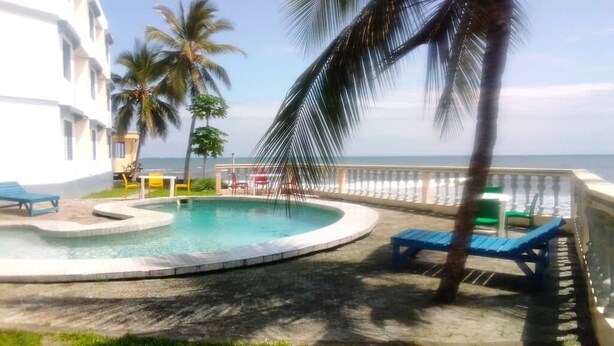 A pool area with lounge chairs and a palm tree, overlooking the ocean. - Hôtel Les Polygones (Kribi)