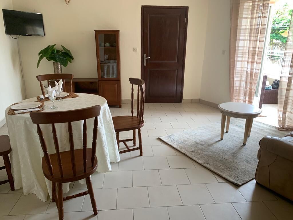 A dining area with a round table, chairs, a cabinet, and a television on the wall.