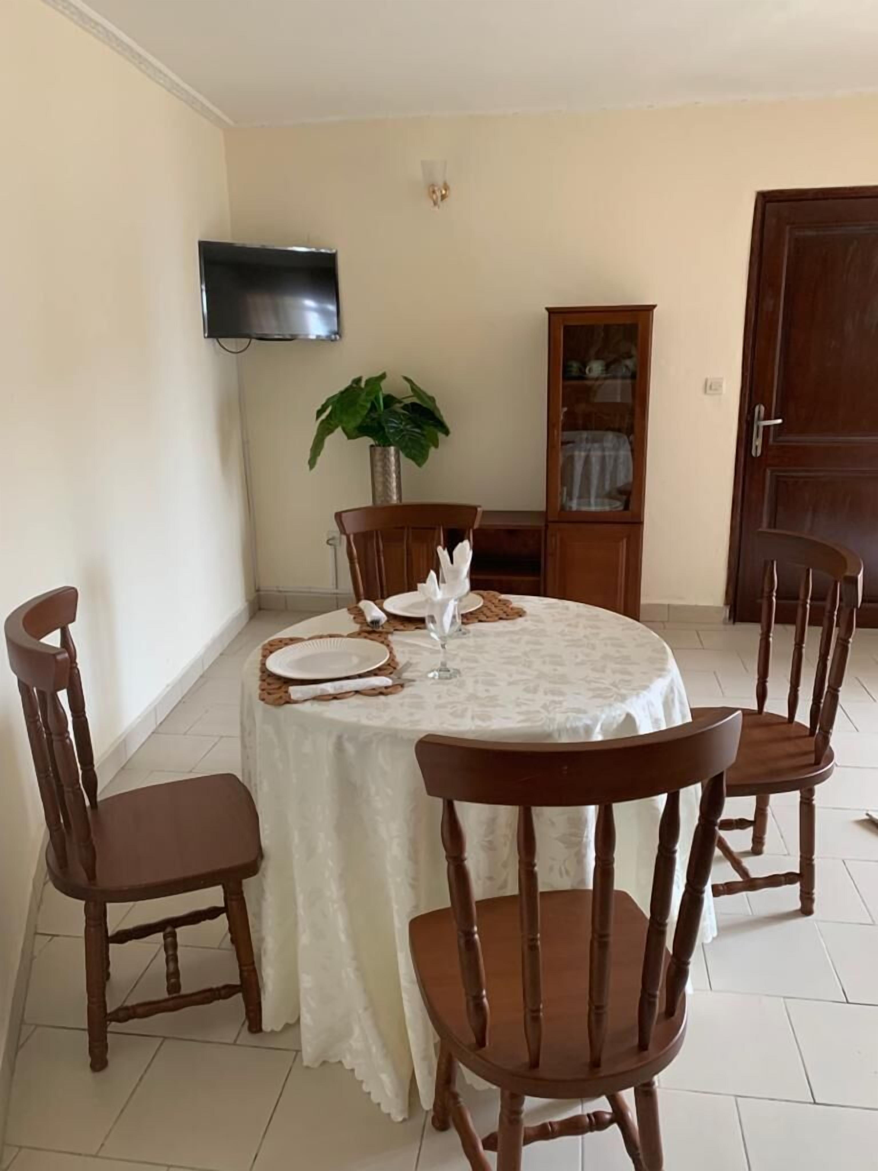 A dining area with a round table, four wooden chairs, a television mounted on the wall, and a cabinet with glass doors.