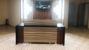 A room with a large flat-screen TV mounted on a wall, a wooden cabinet in the center, and a tiled floor. - Hôtel Les Polygones (Kribi)