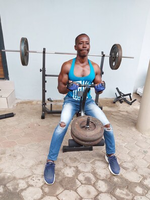 A person seated on a bench, performing a weightlifting exercise with a barbell. - Gem Hospitalities (Accra)