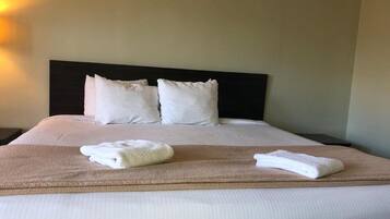A neatly made bed with white linens and two pillows, a brown throw blanket, and two folded towels on the bed.