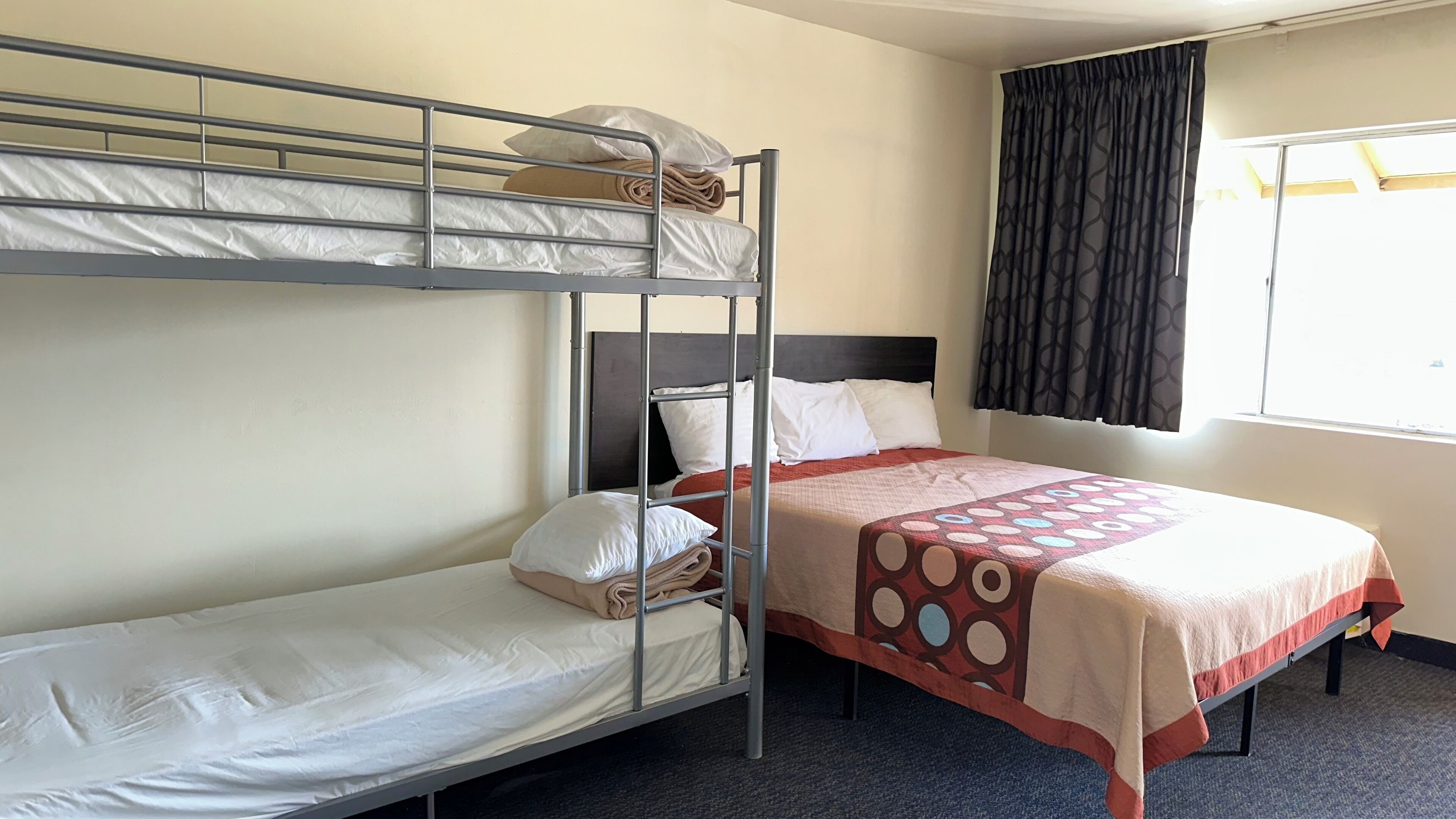 Ein Hotelzimmer mit einem Etagenbett, einem Einzelbett und einem Vorhangfenster.