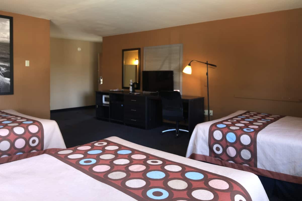 A hotel room with two beds, a desk, a chair, a TV, and a lamp.