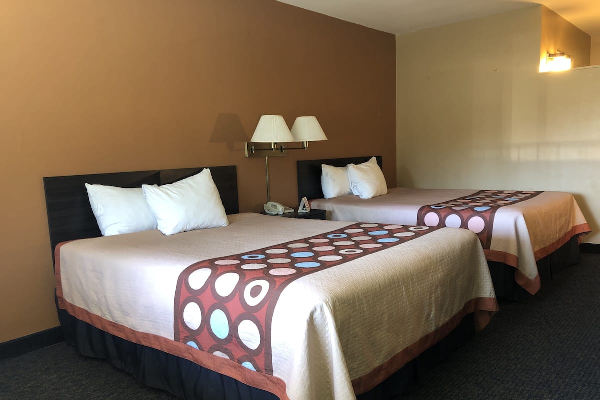 Two beds with white linens and a patterned throw blanket, a bedside lamp, and a phone on the nightstand.