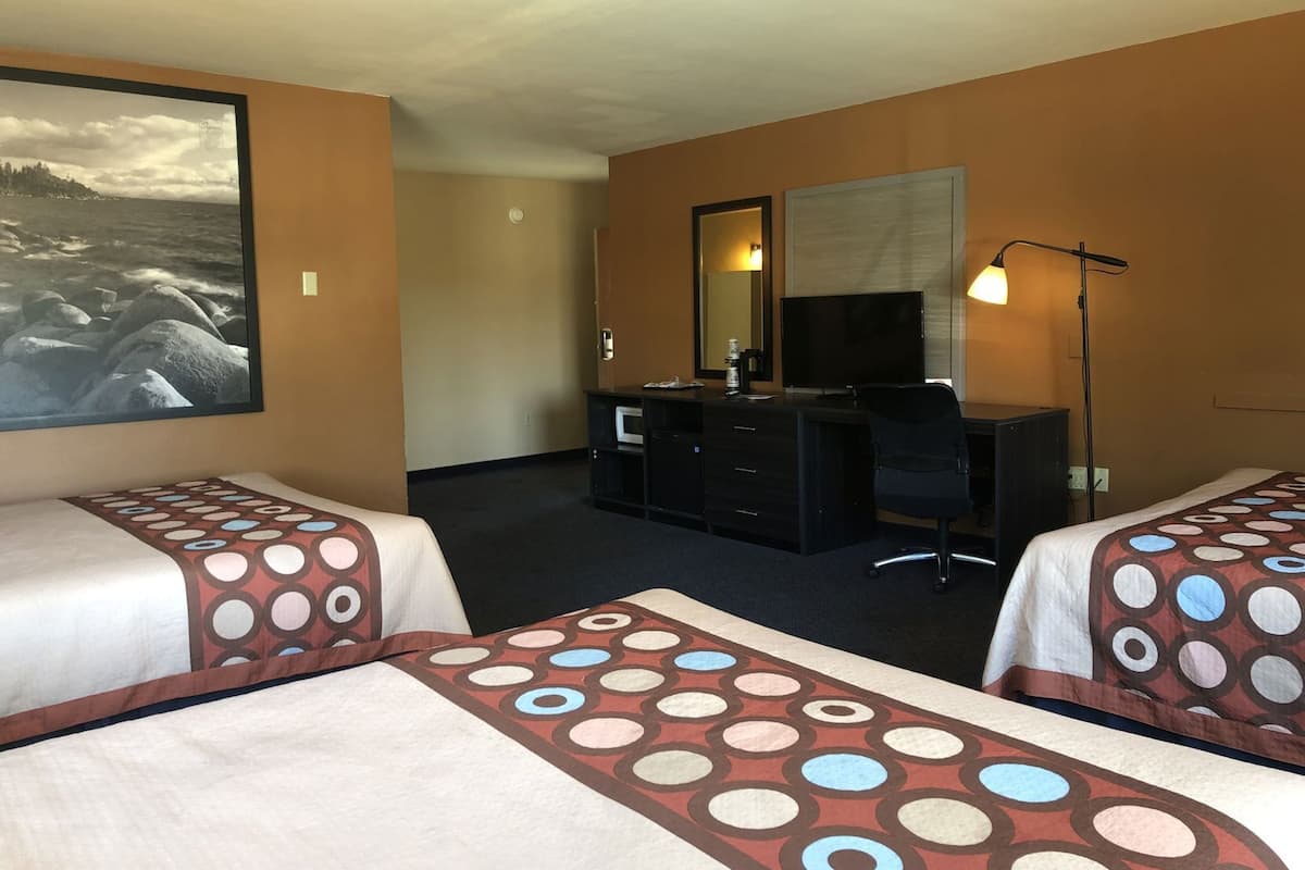 A hotel room with two beds, a desk, a chair, a TV, and a large picture on the wall.