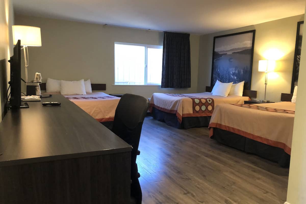 A hotel room with two beds, a desk, a chair, a coffee maker, and a painting on the wall.