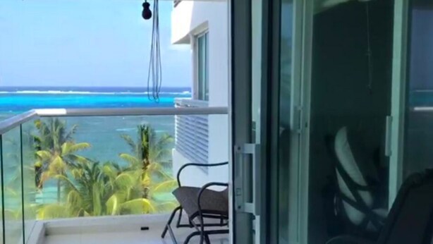 A balcony with a view of the ocean, a chair, and a glass door. - Apartamento Familiar (San Andrés)