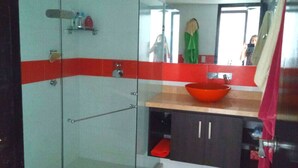 A modern bathroom with a glass shower enclosure, a red and white tiled wall, a wooden countertop, and a red basin. - Apartamento Familiar (San Andrés)