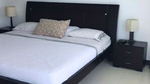 A neatly made bed with a patterned pillow, a dark headboard, and two bedside tables with lamps. - Apartamento Familiar (San Andrés)