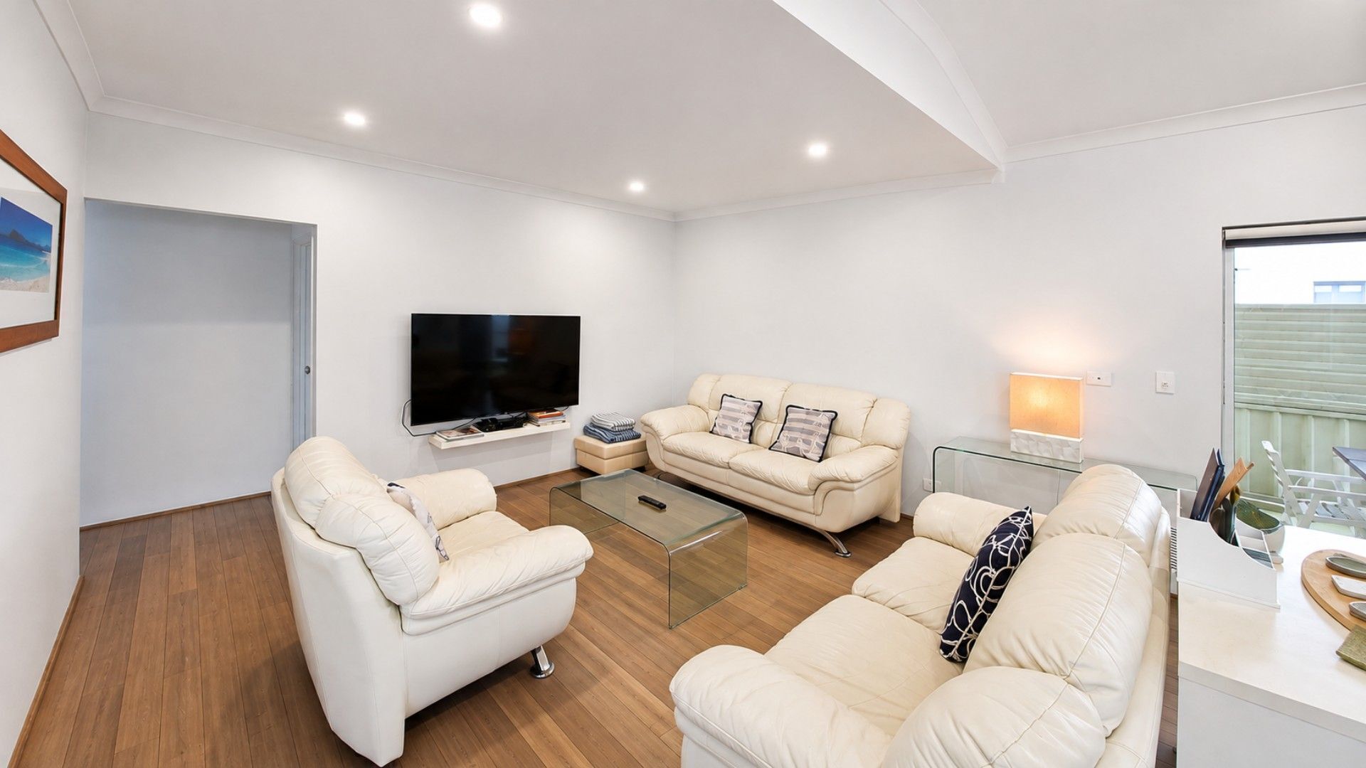 A modern living room with a flat-screen TV, two sofas, a glass coffee table, and a balcony with a railing.