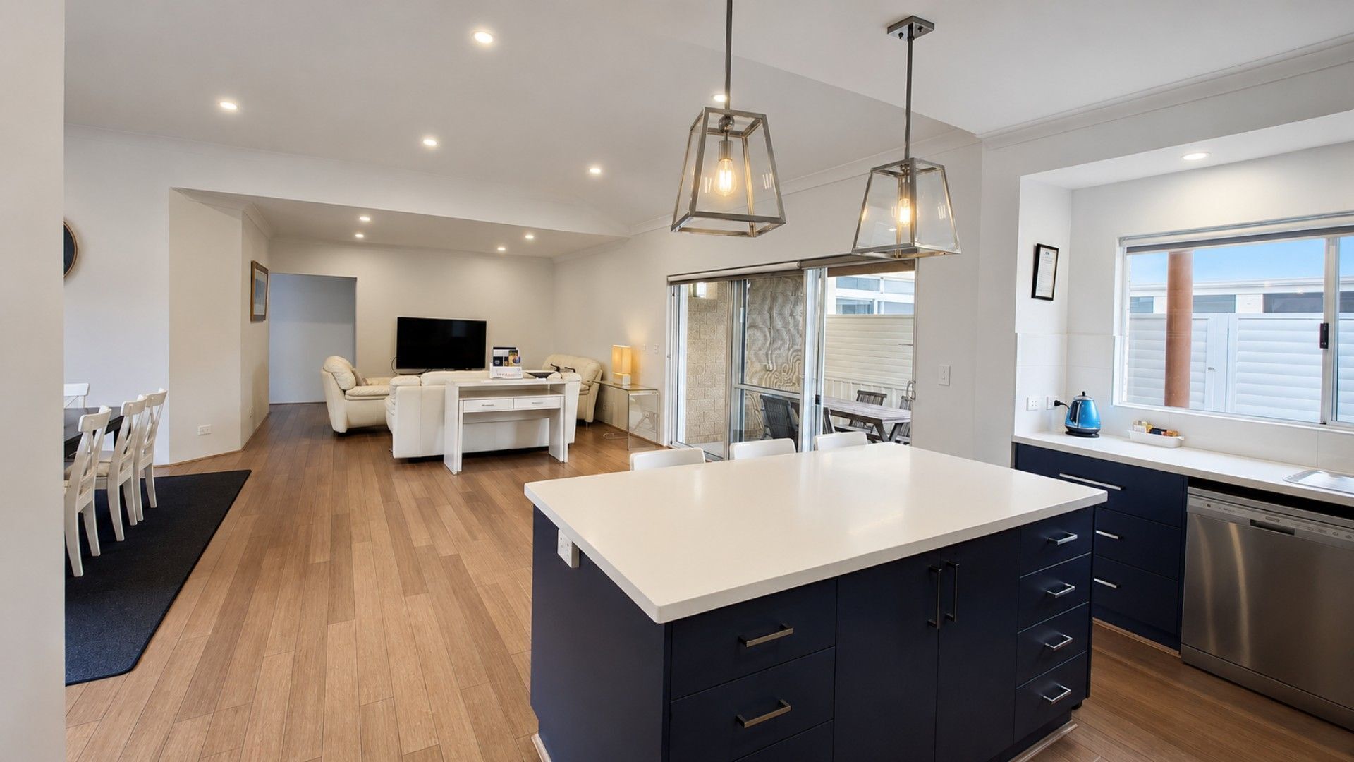 A modern kitchen with a central island, a dining area with a sofa, and a TV in the background.