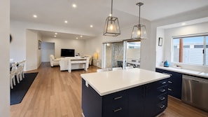 A modern kitchen with a central island, a dining area with a sofa, and a TV in the background.