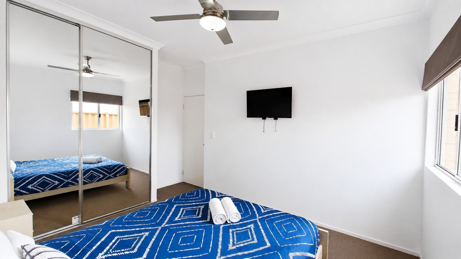 A bedroom with a bed, a ceiling fan, a TV, and a window.