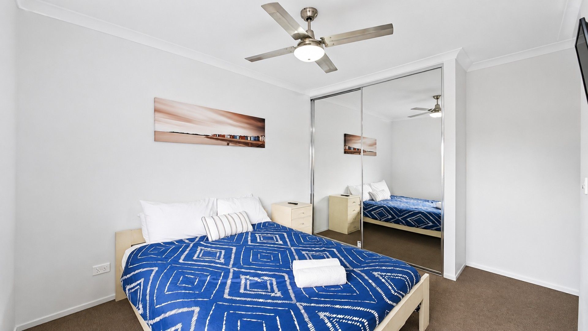 Une chambre à coucher comprenant un lit, une table de chevet, une commode, un ventilateur de plafond et un grand miroir.
