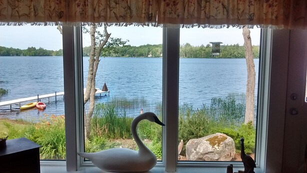 En svanfigur på en fönsterbräda med utsikt över en sjö, en brygga och träd.