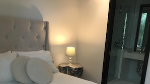 Una cama bien hecha con cabecera, una lámpara de noche y una mesita de noche de madera.
