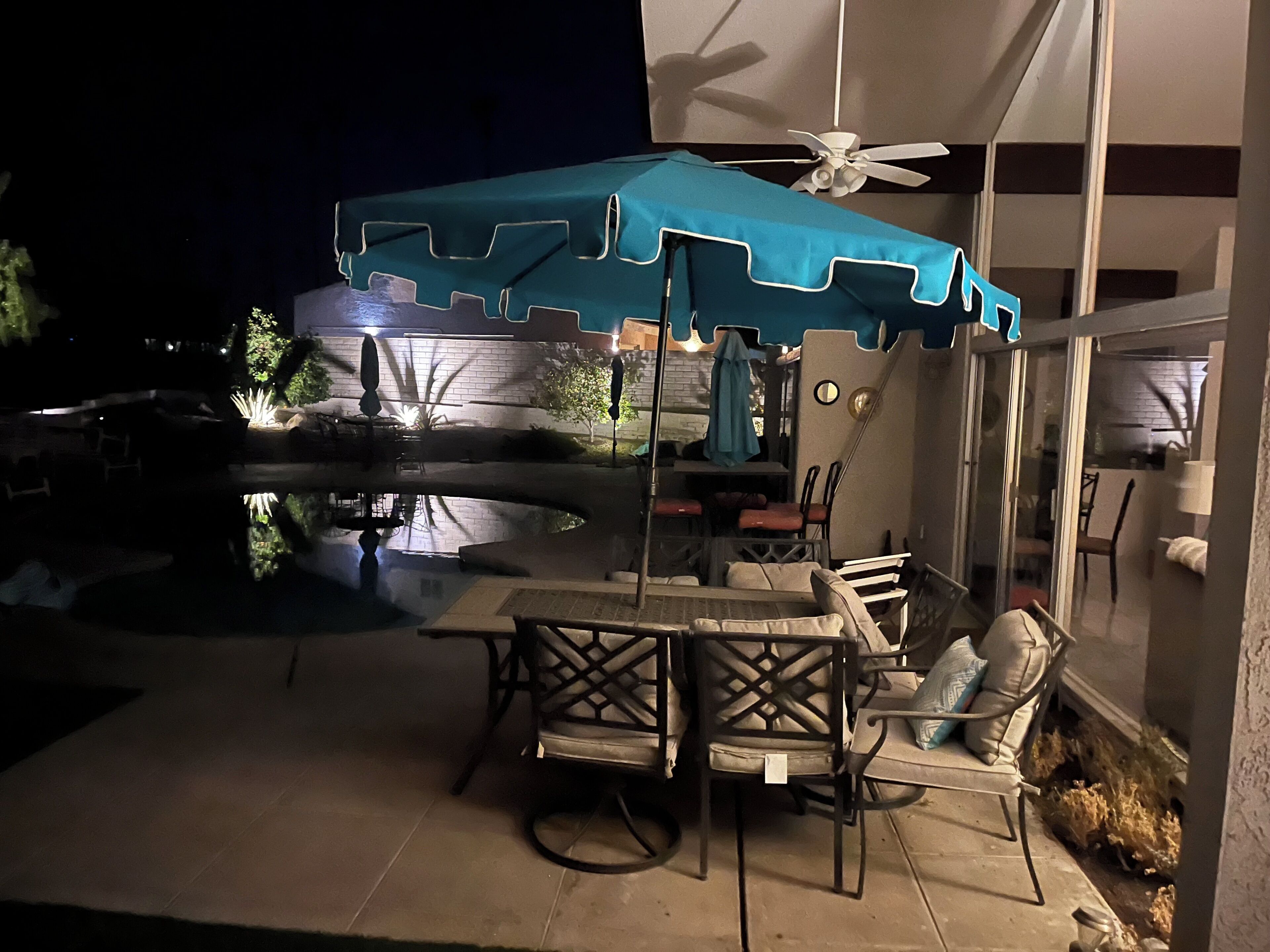 An outdoor patio with a table and chairs, a ceiling fan, and a pool.