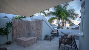 A covered outdoor seating area with a built-in bench, wicker chairs, and a potted plant.