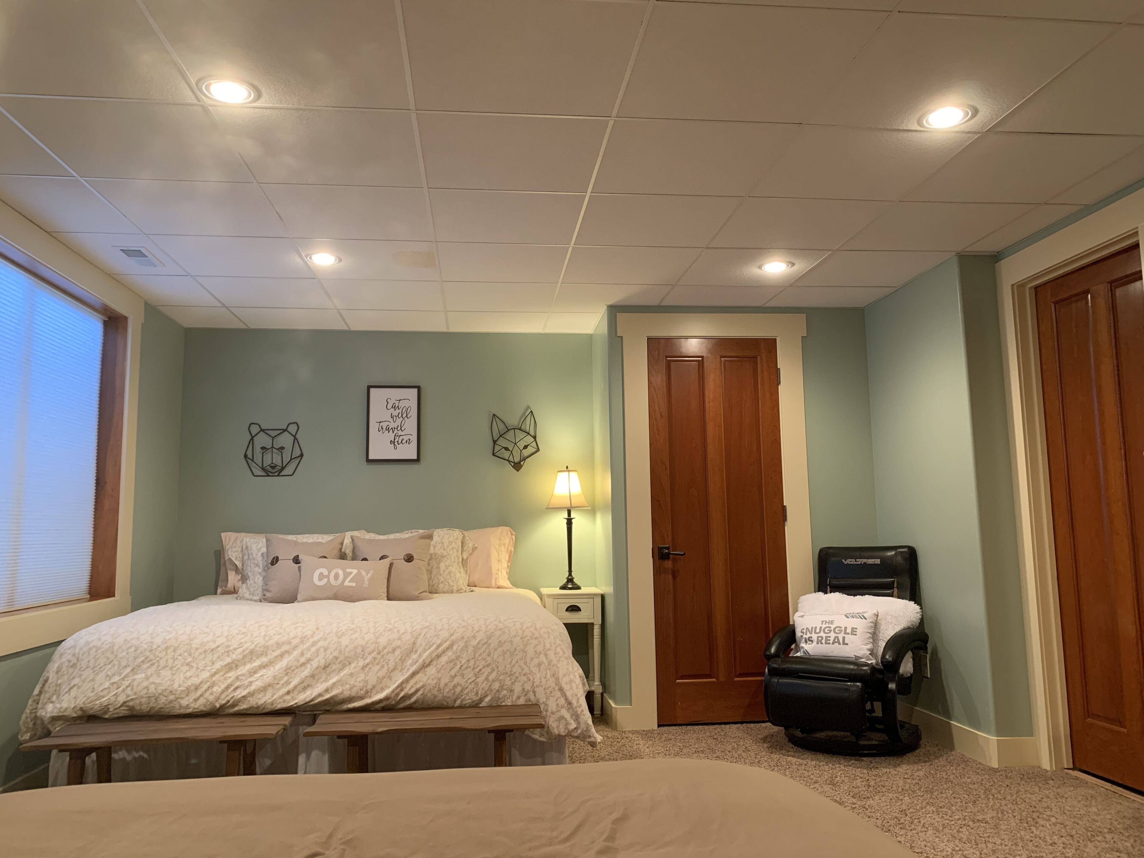 A bedroom with a bed, a bench, a wall-mounted lamp, and a door.