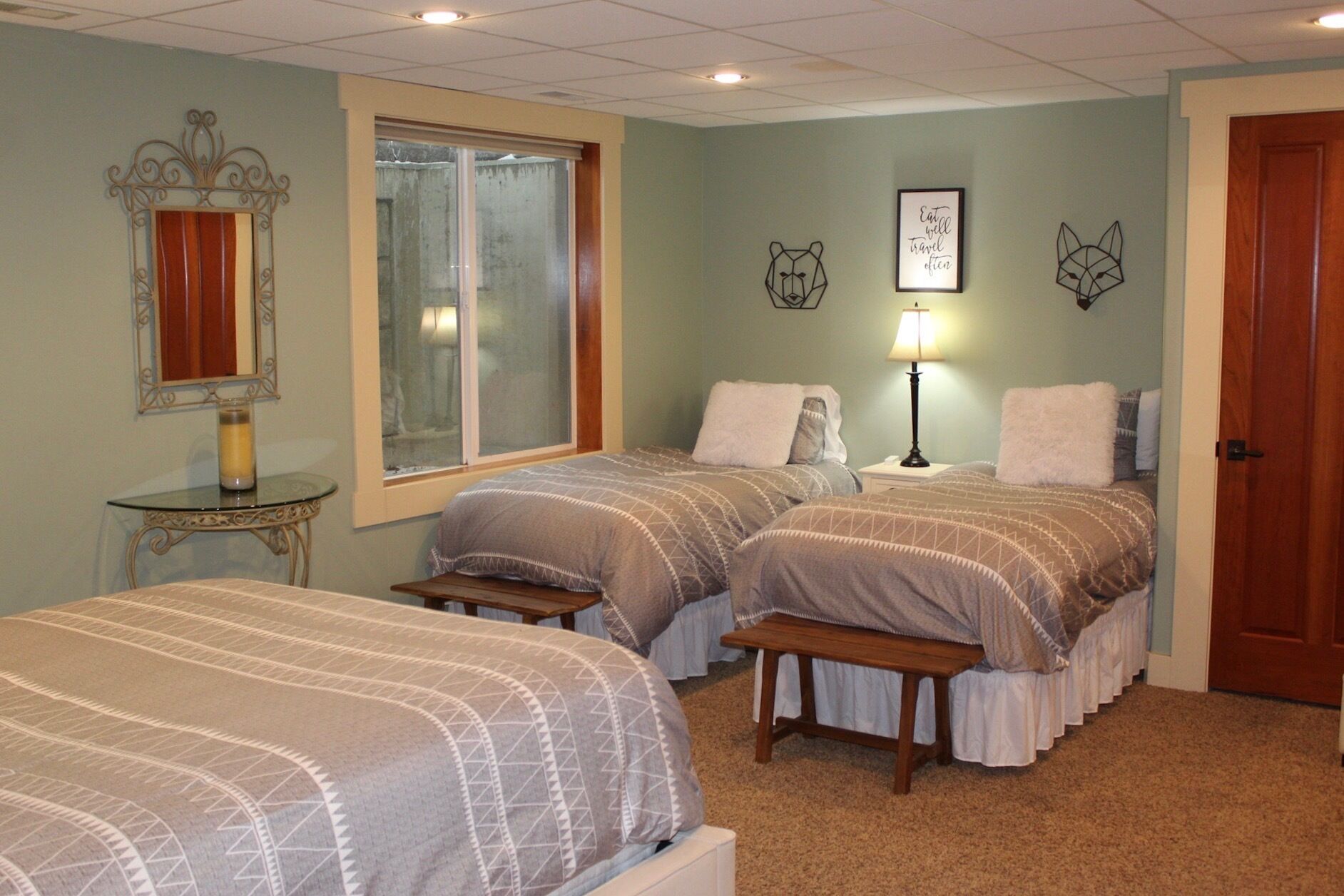 A bedroom with two beds, a window, a mirror, and a door.