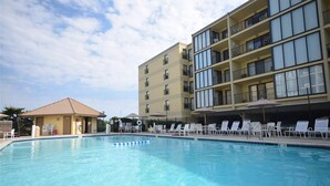 A swimming pool with lounge chairs, a building with multiple balconies, and a small structure with a roof.