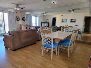 Un vaste espace de vie comprenant un canapé marron, une table à manger avec des chaises à coussins bleus et un ventilateur de plafond.