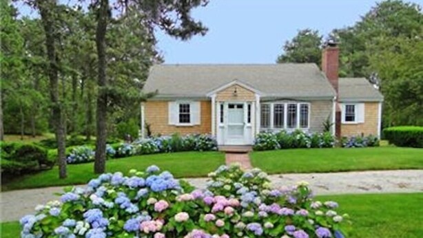 A two-story house with a front porch, surrounded by a well-maintained lawn and flowering bushes. - Chatham-Walk to Ridgevale Beach, Winter Rental Option (Chatham)