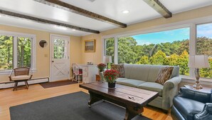 A living room with a wooden coffee table, a sofa, and a couch. There is a door and a window with a view of trees. - Chatham-Walk to Ridgevale Beach, Winter Rental Option (Chatham)