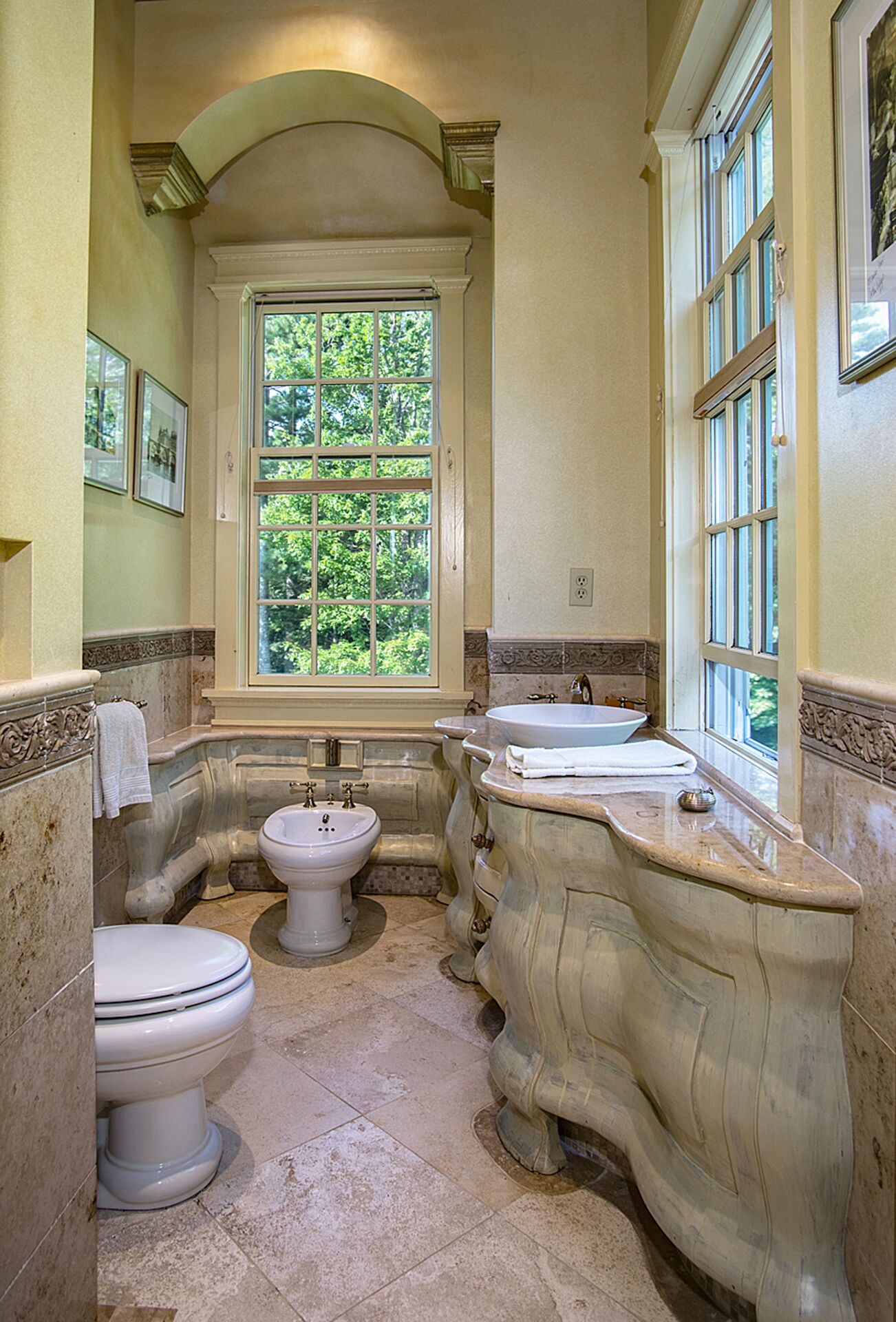 Un baño con un ventanal amplio, un lavamanos y dos inodoros.