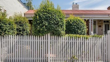 Stunning home with a charming white picket fence, brick chimney, and lush green surroundings.