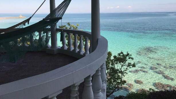 Un balcon avec un hamac, d’où l’on peut admirer une mer d’un bleu limpide et une île lointaine.