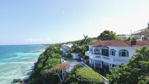 Une propriété située sur la côte, avec une grande maison dotée d’un toit recouvert de tuiles rouges, d’une piscine et d’une vue sur l’océan.