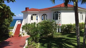 Un bâtiment blanc avec un toit rouge, un escalier menant à l’entrée et une vue sur l’océan.