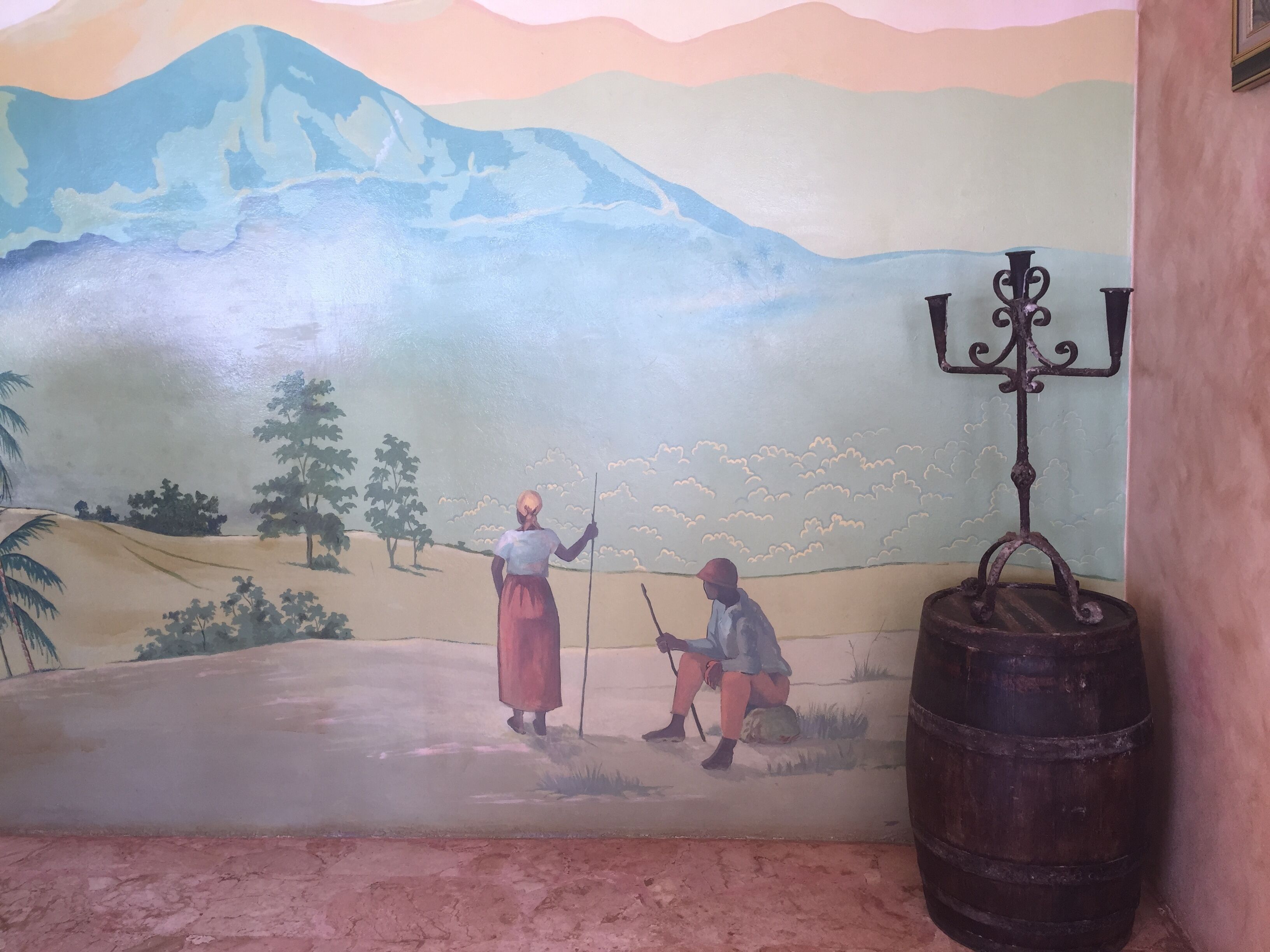 Une fresque représentant une scène pastorale avec deux personnages, l’un debout et l’autre assis, dans un cadre rural avec une montagne en arrière-plan.
