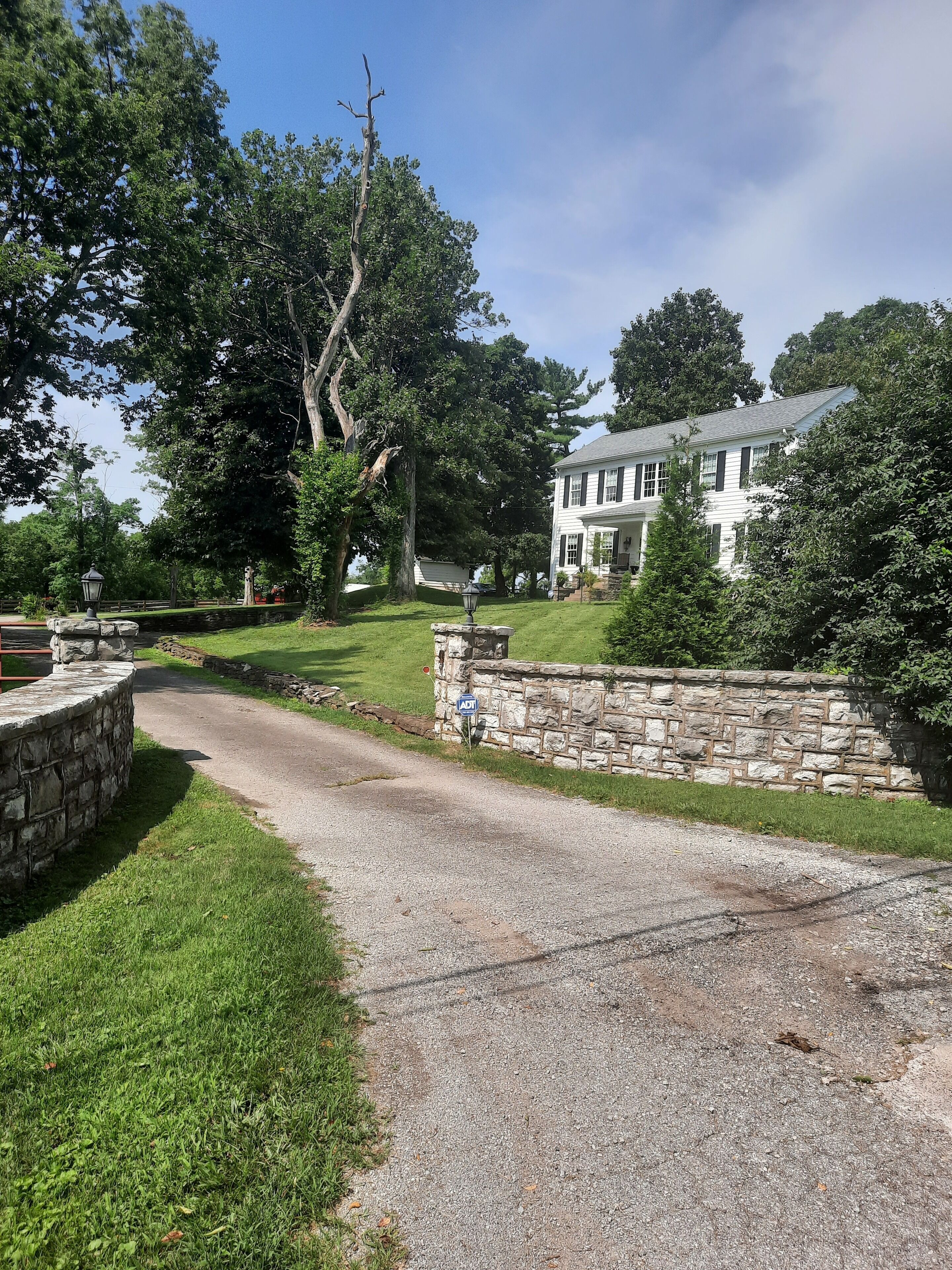 A two-story house with a stone wall and a paved driveway.