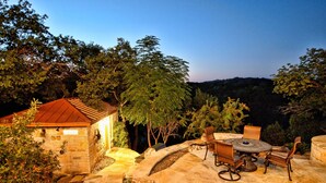 Une terrasse en pierre avec des meubles d’extérieur, un bâtiment en pierre et des arbres environnants.