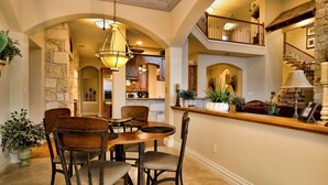 Une salle à manger spacieuse avec un plafond haut, des murs en pierre et une vue sur la cuisine et l’étage supérieur.