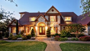 Une grande maison en pierre à deux étages, dotée d’une pelouse bien entretenue et d’une allée en gravier menant à l’entrée.