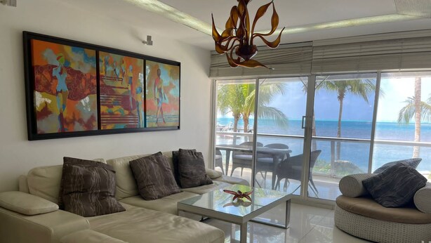 A modern living room with a beige sofa, a glass coffee table, and a view of the ocean through large windows. - Modern Apartment in Torres del Sunrise (San Andrés)