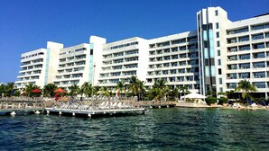 A large hotel with multiple floors and balconies, a dock with lounge chairs, and palm trees. - Modern Apartment in Torres del Sunrise (San Andrés)