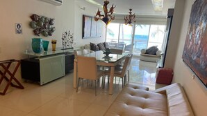 A modern living room with a glass dining table, beige sofa, and a view of the ocean through large windows. - Modern Apartment in Torres del Sunrise (San Andrés)