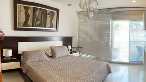 A modern bedroom with a large bed, a nightstand with a lamp, a small table, and a large window with blinds. - Modern Apartment in Torres del Sunrise (San Andrés)