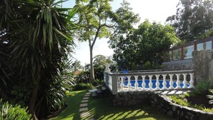 A garden with a pool, stone wall, and a white chair. - Madeiran Quinta with a wonderful 4000 m2 Botanical Garden with private pool (S.Gonçalo)