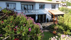 A two-story house with a balcony, surrounded by lush greenery and flowering plants. - Madeiran Quinta with a wonderful 4000 m2 Botanical Garden with private pool (S.Gonçalo)