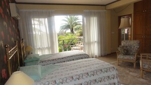 A hotel room with two beds, a balcony with curtains, a chair, and a wardrobe. - Madeiran Quinta with a wonderful 4000 m2 Botanical Garden with private pool (S.Gonçalo)